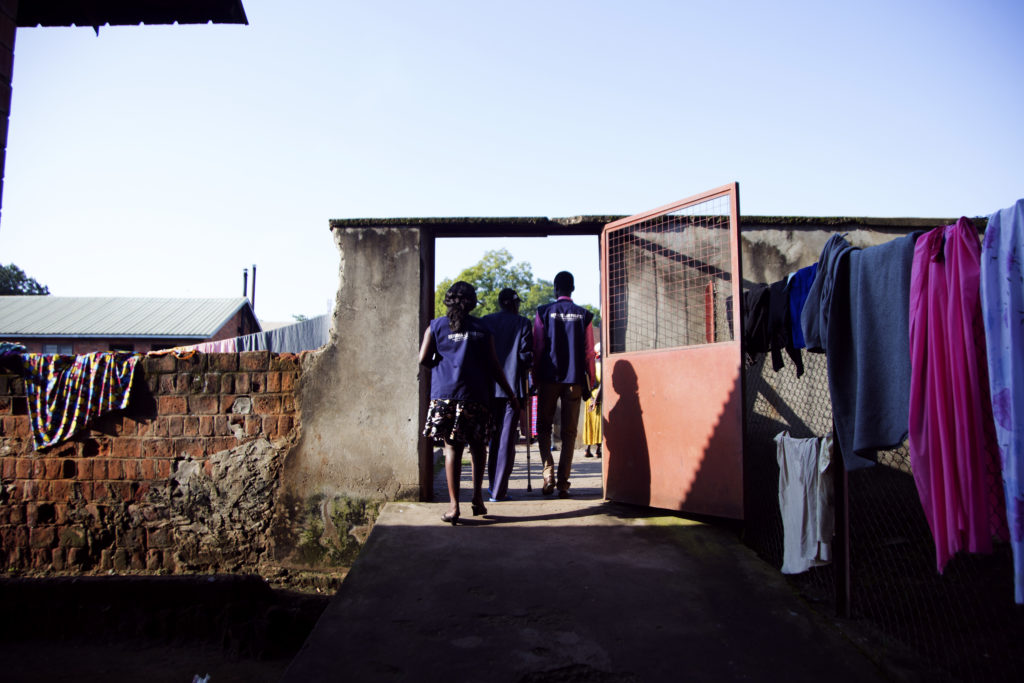 John is escorted out of Lacor hospital patients' shelter by Refugee Law Project officers to go see the Doctor for a follow up treatment appointment. This is at about 10am in the morning. 